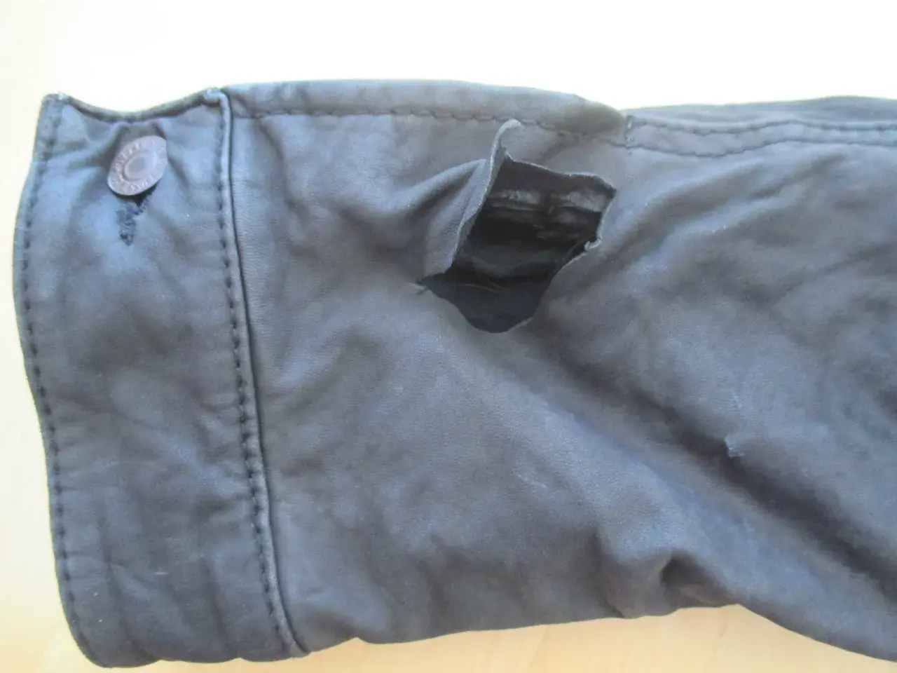 Gros accroc sur un vêtement en cuir, révélant la doublure intérieure. Le bouton sur le côté gauche est intact.