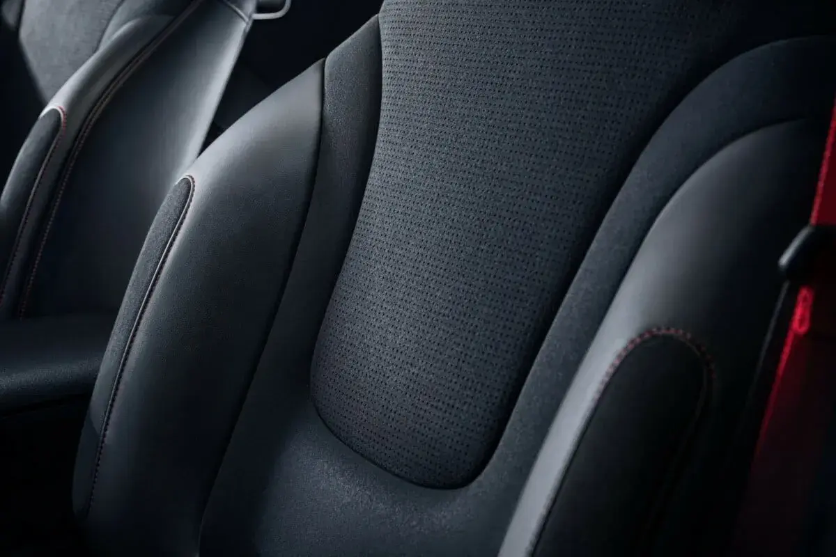 Sièges de voiture en cuir noir et matière alcantara, avec surpiqûres rouges contrastantes.