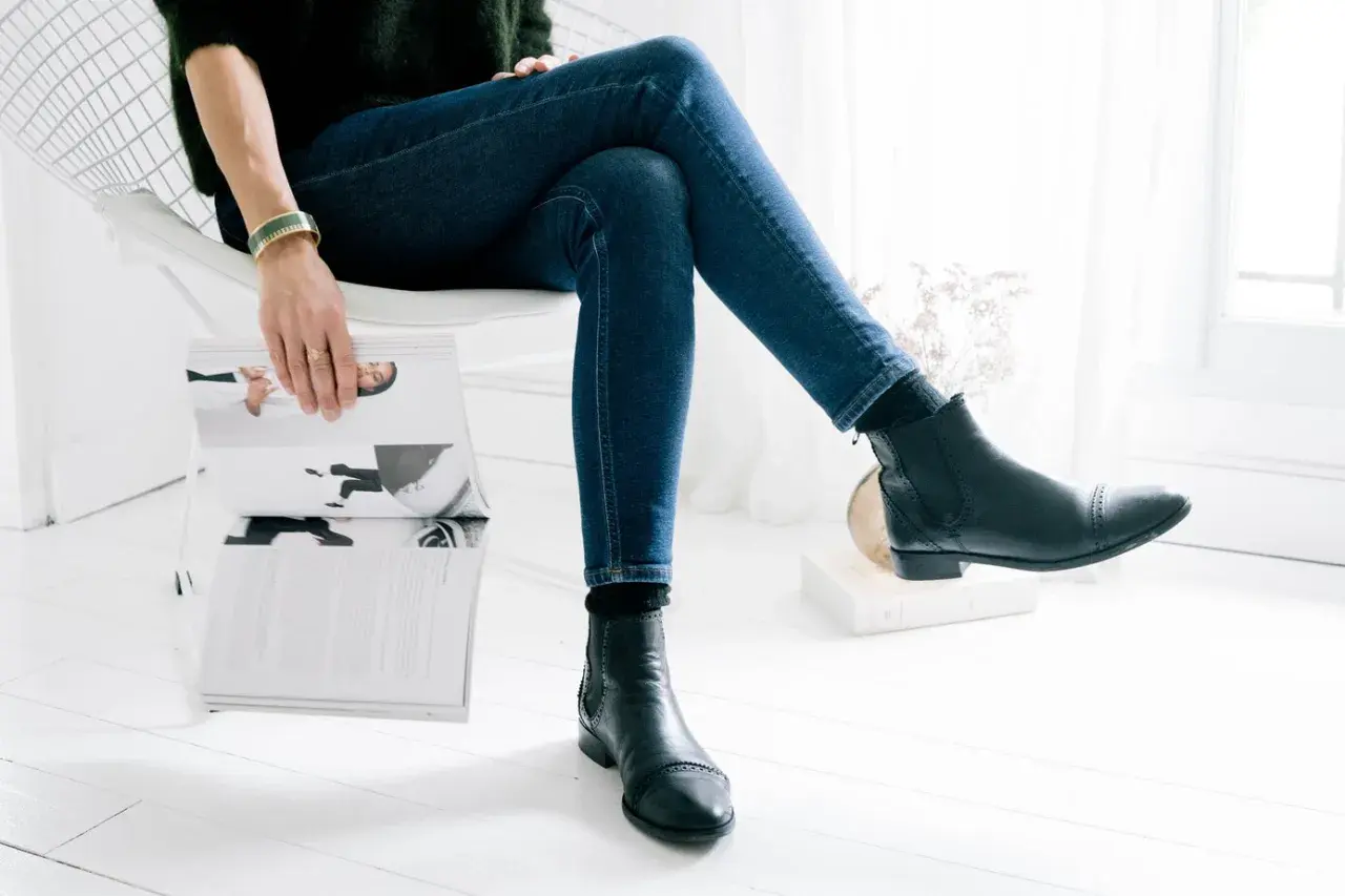 Une femme assise lit un magazine, portant un jean slim et des bottines Chelsea noires.