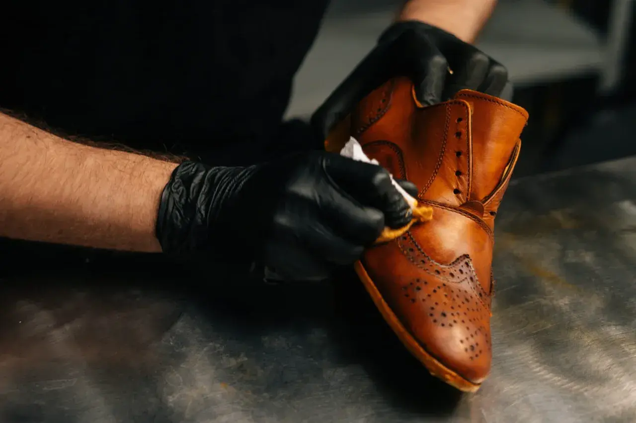 Gants noirs pour un entretien simili cuir. Un homme nettoie une chaussure marron avec un chiffon.