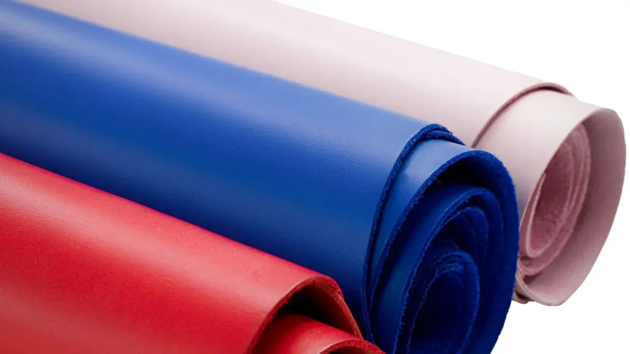 Rouleaux de cuir coloré, rouge, bleu et rose pâle, évoquant la douceur d'une vachette animal.
