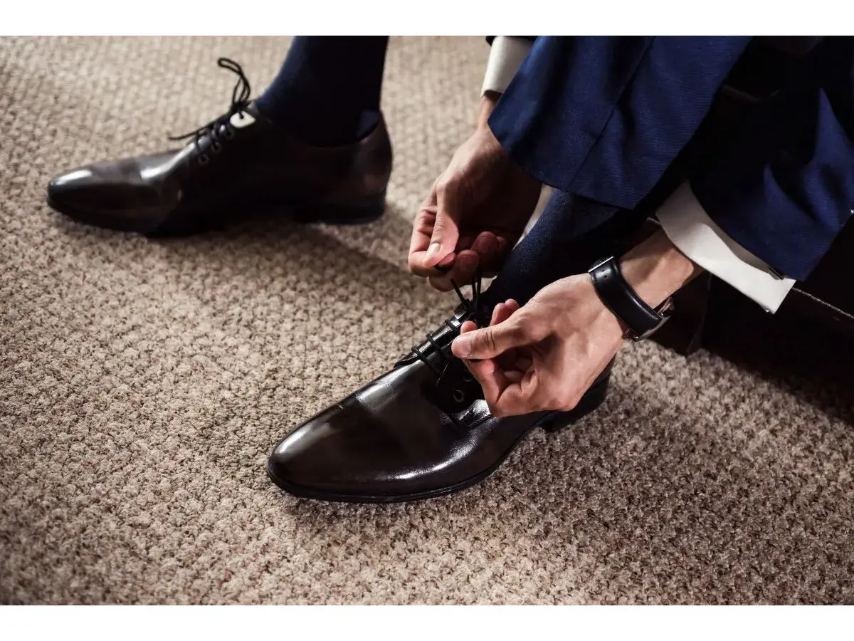 Un homme en costume bleu marine attache ses chaussures vernies marron. Quel chaussure avec un costume pour un look impeccable.
