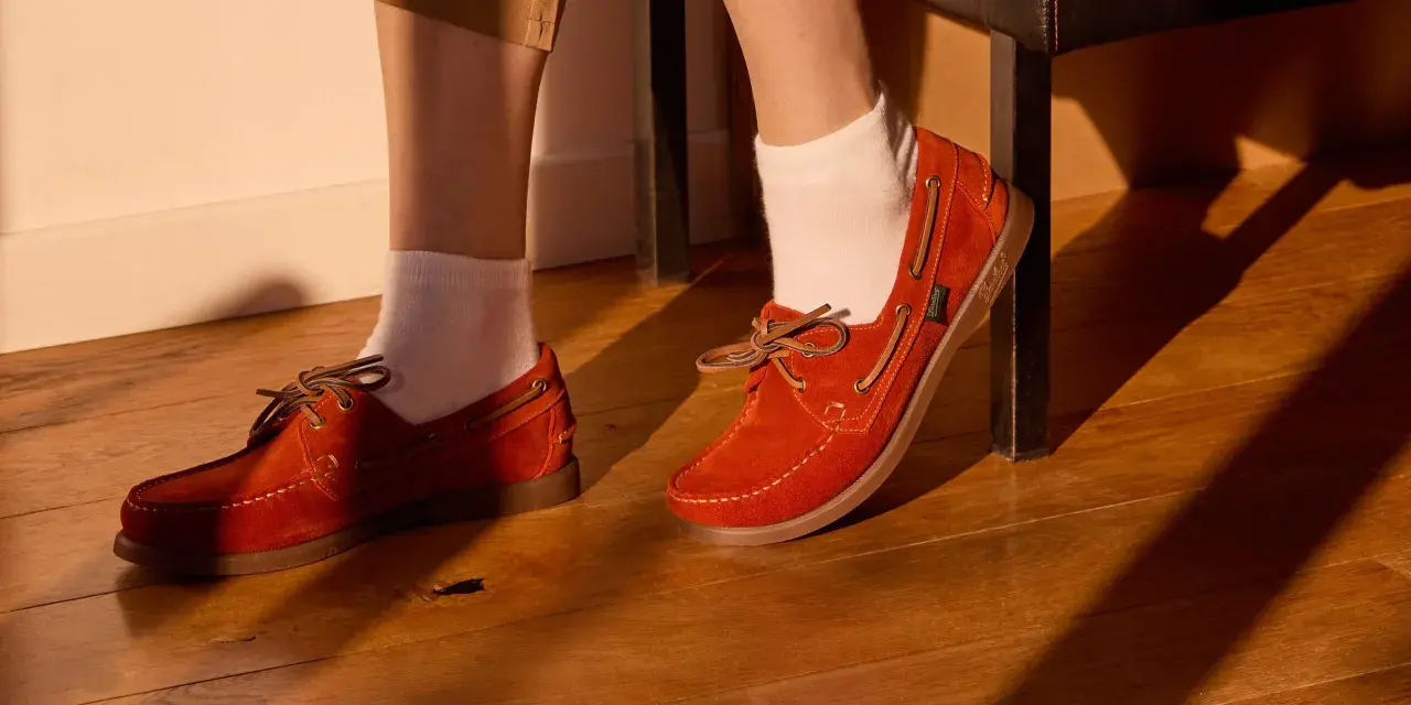 Chaussure bateau femme look : des mocassins en daim orange vif avec lacets en cuir, portés avec des chaussettes blanches sur un parquet en bois.