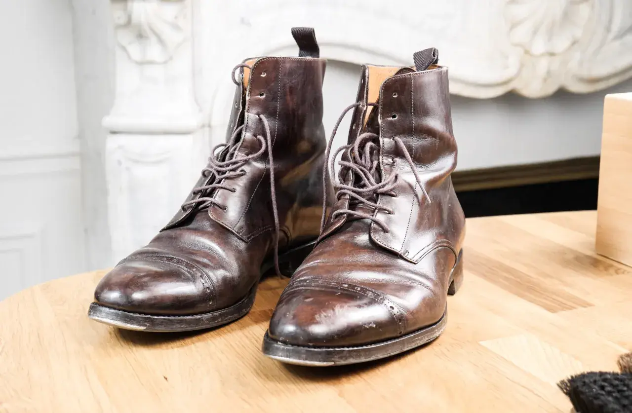 Paire de bottines en cuir griffé marron foncé, lacets serrés, posées sur une table en bois.