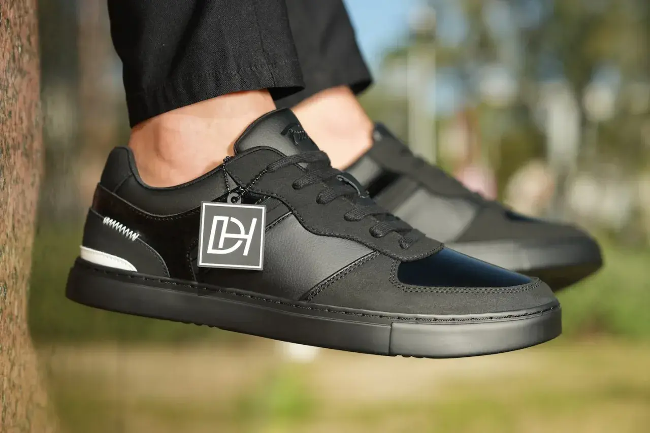 Baskets noires stylées, avec un jean qui détient sur la chaussure. Logo DH sur une étiquette.