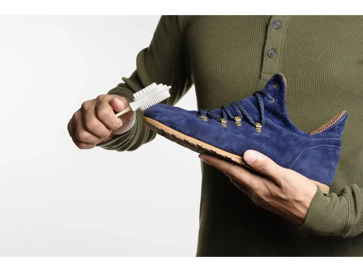 Maintenir le cuir suédé en bon état : une main brosse une chaussure bleue avec une brosse spéciale.