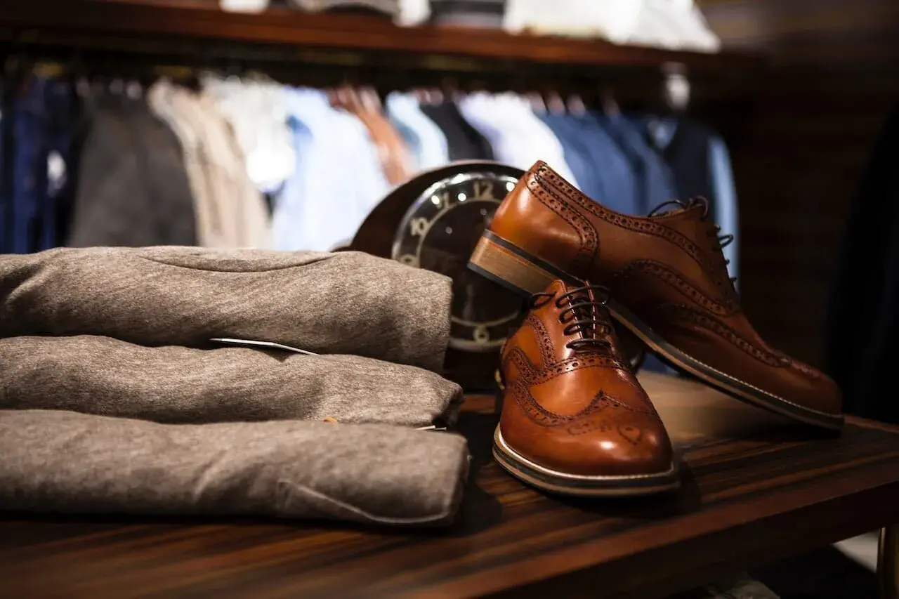 Chaussures en cuir marron élégantes, prêtes à être assouplies. Un pull plié et un manteau sont visibles en arrière-plan.