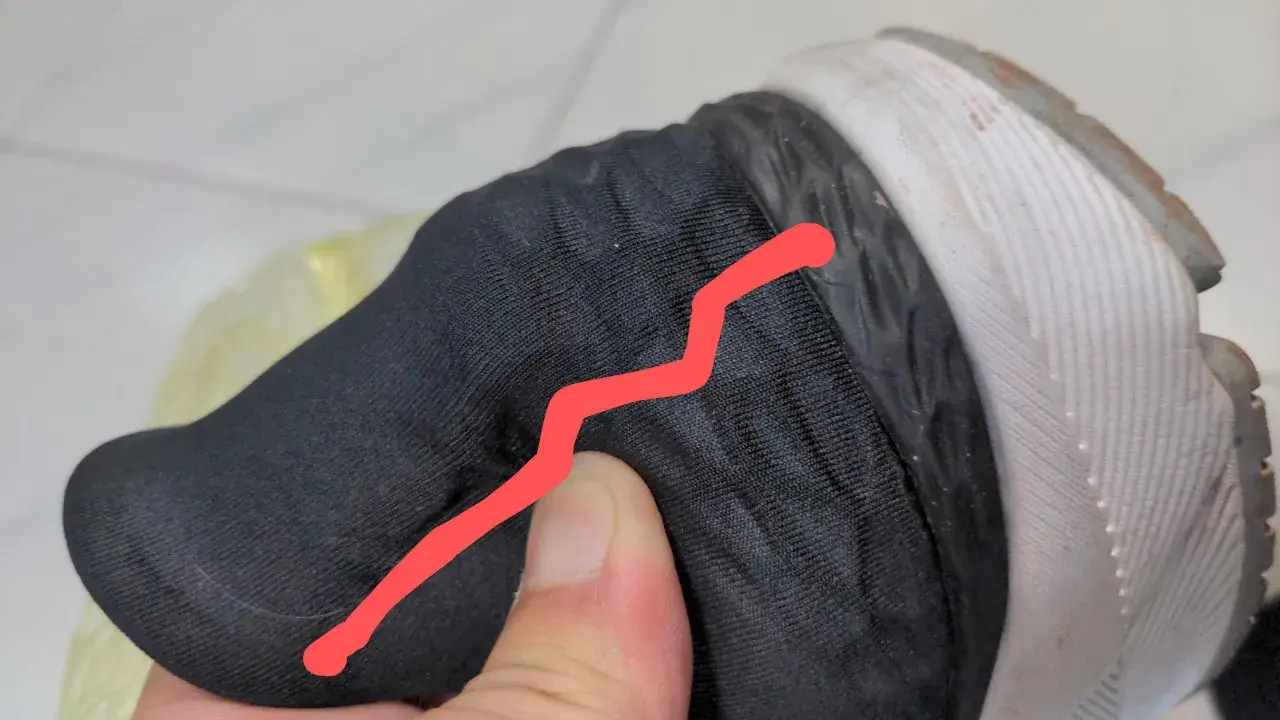 Un pouce appuie sur le contrefort d'une chaussure noire, révélant une fissure.