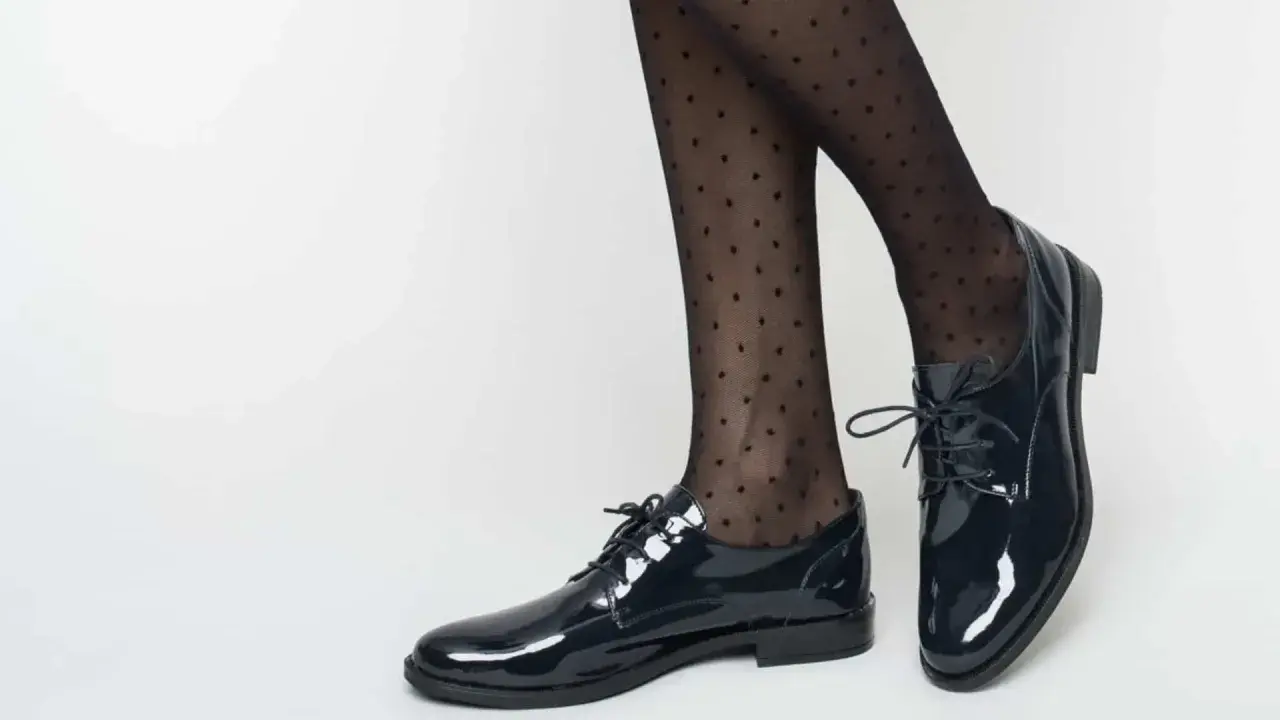 Pieds chaussés de derbies vernies et collants à pois. Idéal pour savoir comment porter des derbies femme avec élégance.