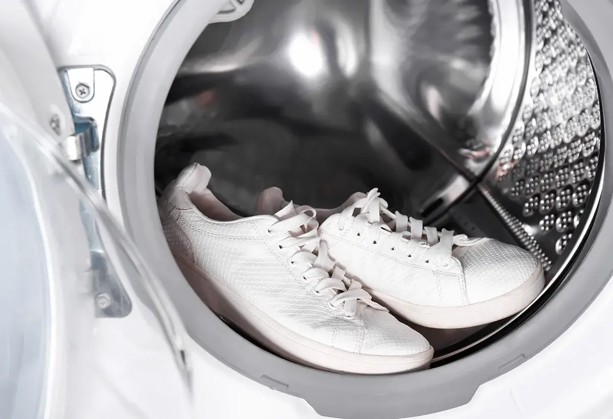 Paire de baskets blanches dans le tambour d'une machine à laver.