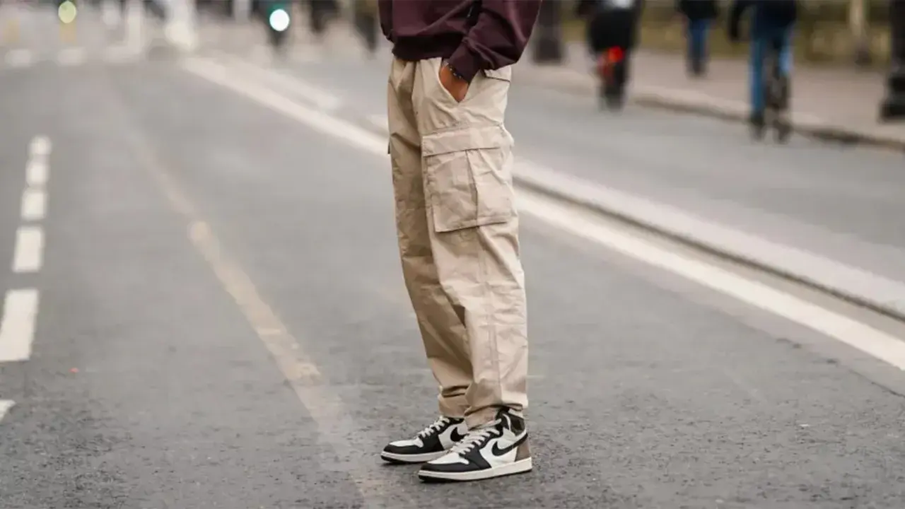 Un homme porte un pantalon cargo beige et une chaussure de sport iconique, prêt pour une journée en ville.