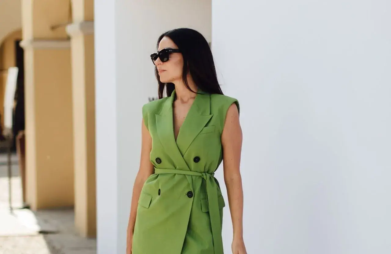 Une femme en robe blazer verte, lunettes de soleil, incarne pourquoi bien s'habiller au travail : confiance et professionnalisme.