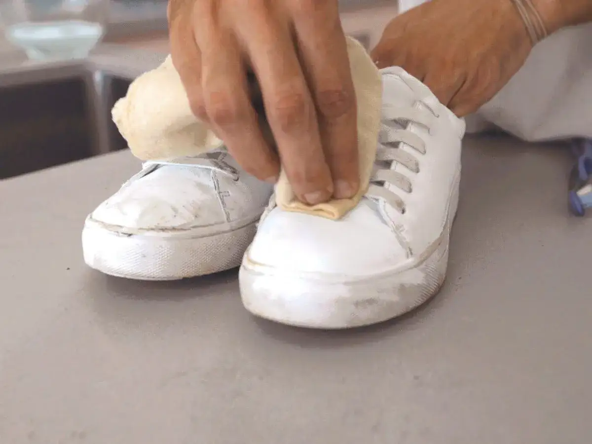 Main d'une personne en train de nettoyer du cuir blanc jauni sur une basket avec un chiffon.