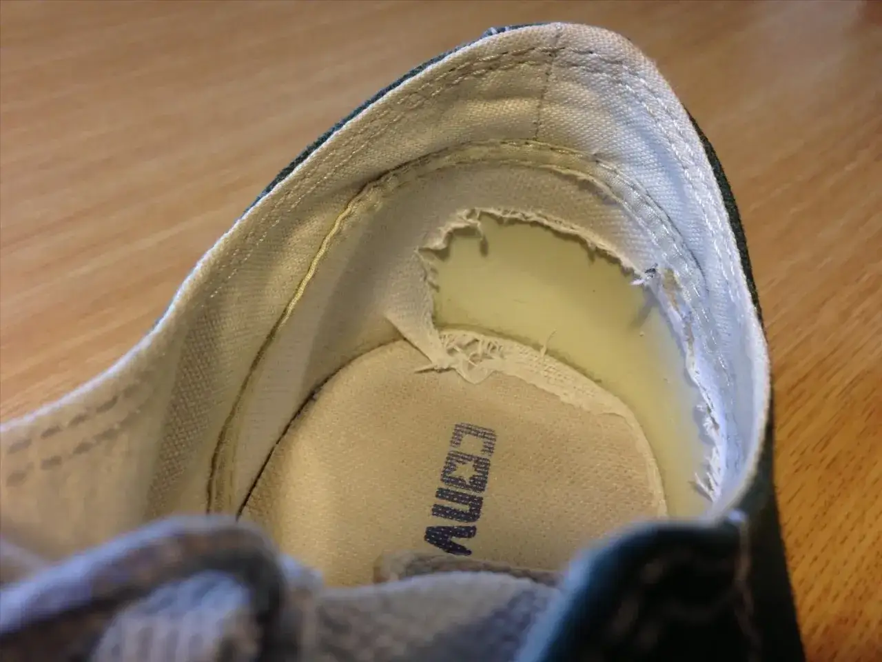 Vue rapprochée de l'intérieur d'une chaussure montrant une usure anormale du talon, avec le tissu déchiré.