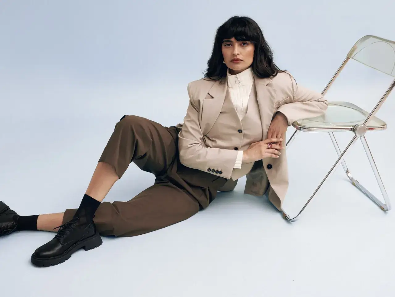 Une femme en tailleur beige et pantalon marron, prête pour un entretien d'embauche femme, porte des chaussures noires à lacets et semelles épaisses.