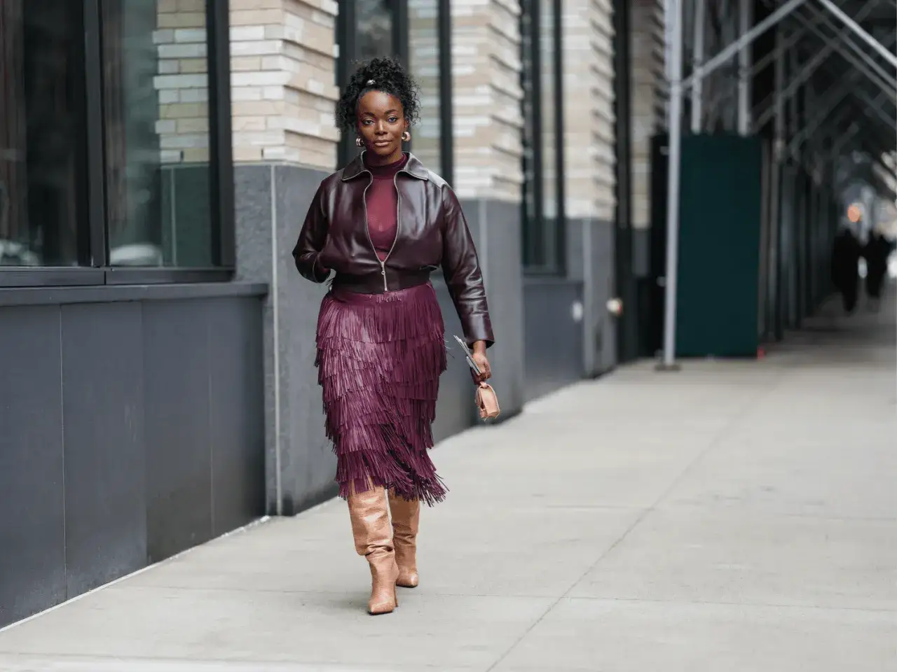 Une femme arbore une élégante association couleur bordeaux pour ses vêtements : veste en cuir, jupe à franges et bottes.