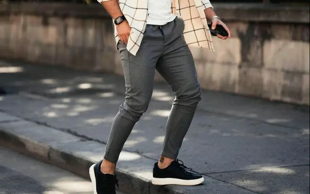 Un homme porte un pantalon gris élégant avec des baskets noires. Quelle chaussure avec pantalon gris homme pour un look décontracté et chic.