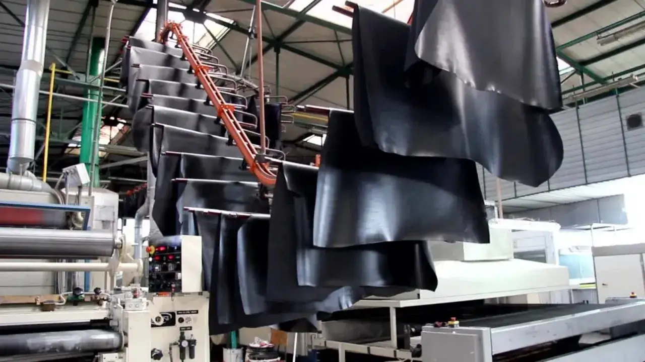 Grandes pièces de cuir noir pendent sur un convoyeur, étape clé du tannage du cuir dans une usine.