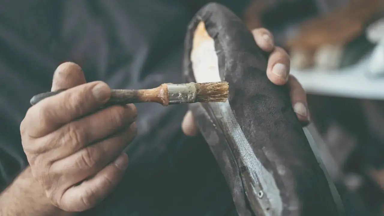Un artisan applique de la colle sur une chaussure, révélant comment est fait le cuir.