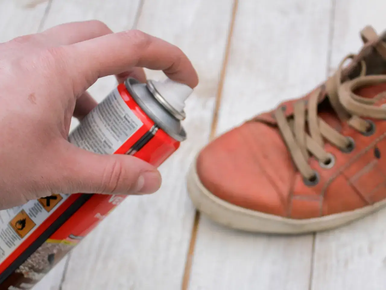 Main tenant une bombe aérosol pour réparer le simili cuir qui s'effrite sur une chaussure orange.