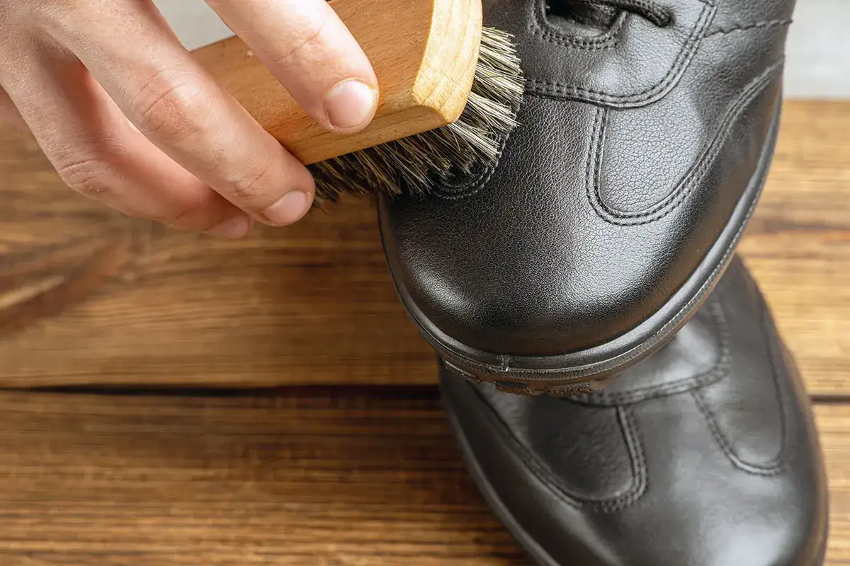 Maintenir l'éclat de vos chaussures en cuir noir. Une main utilise une brosse pour appliquer du cirage, redonnant vie au cuir.