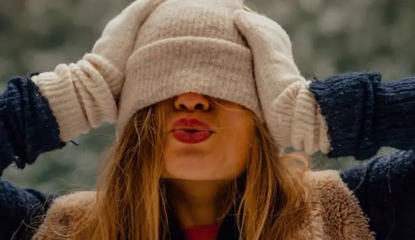 Une jeune femme s'amuse à s'habiller chaudement pour affronter le froid, cachant son visage sous un bonnet et des moufles.