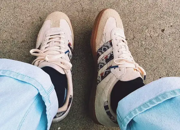 Un homme porte des sneakers Adidas beige avec des détails ethniques, un outfit décontracté parfait pour la belle saison.